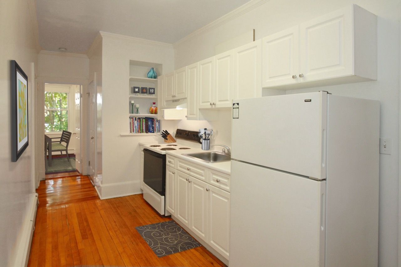White kitchen with fridge, stove, sink, and cabinets in an apartment.