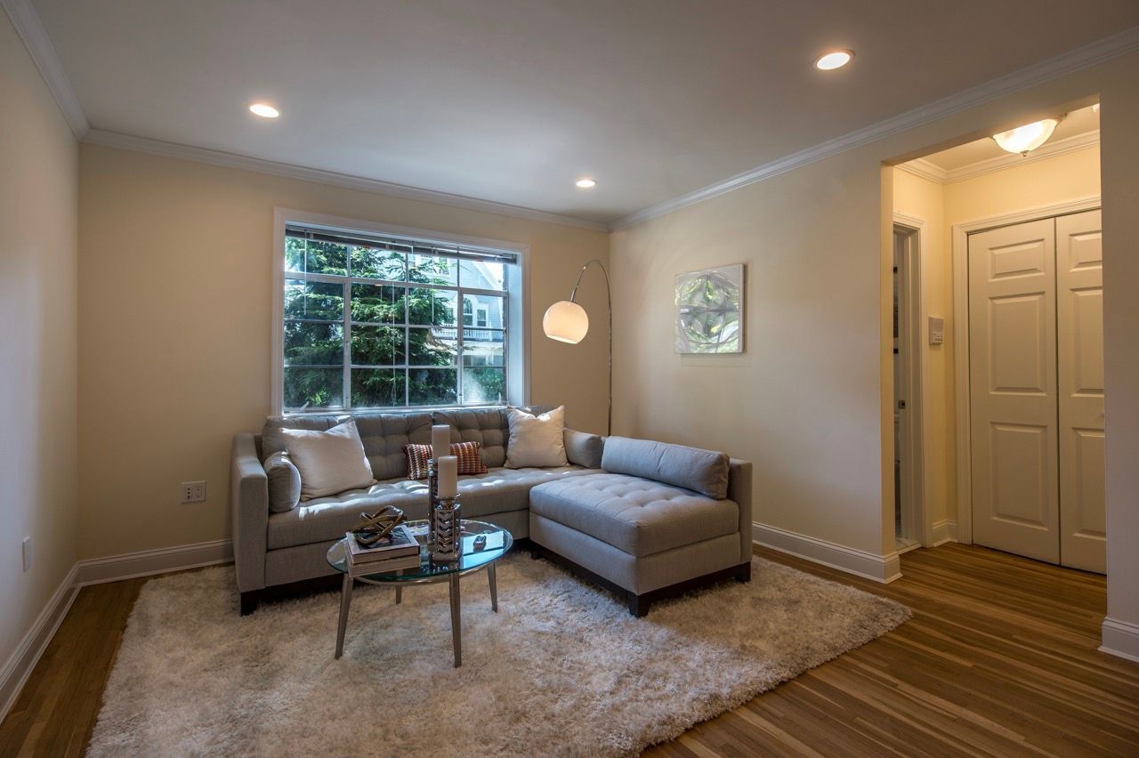 Modern apartment living room with a gray sectional sofa, glass coffee table, white shag rug, and large window.
