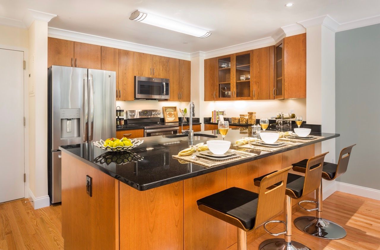 Modern apartment kitchen with wood cabinets, stainless appliances, and a dark granite island.