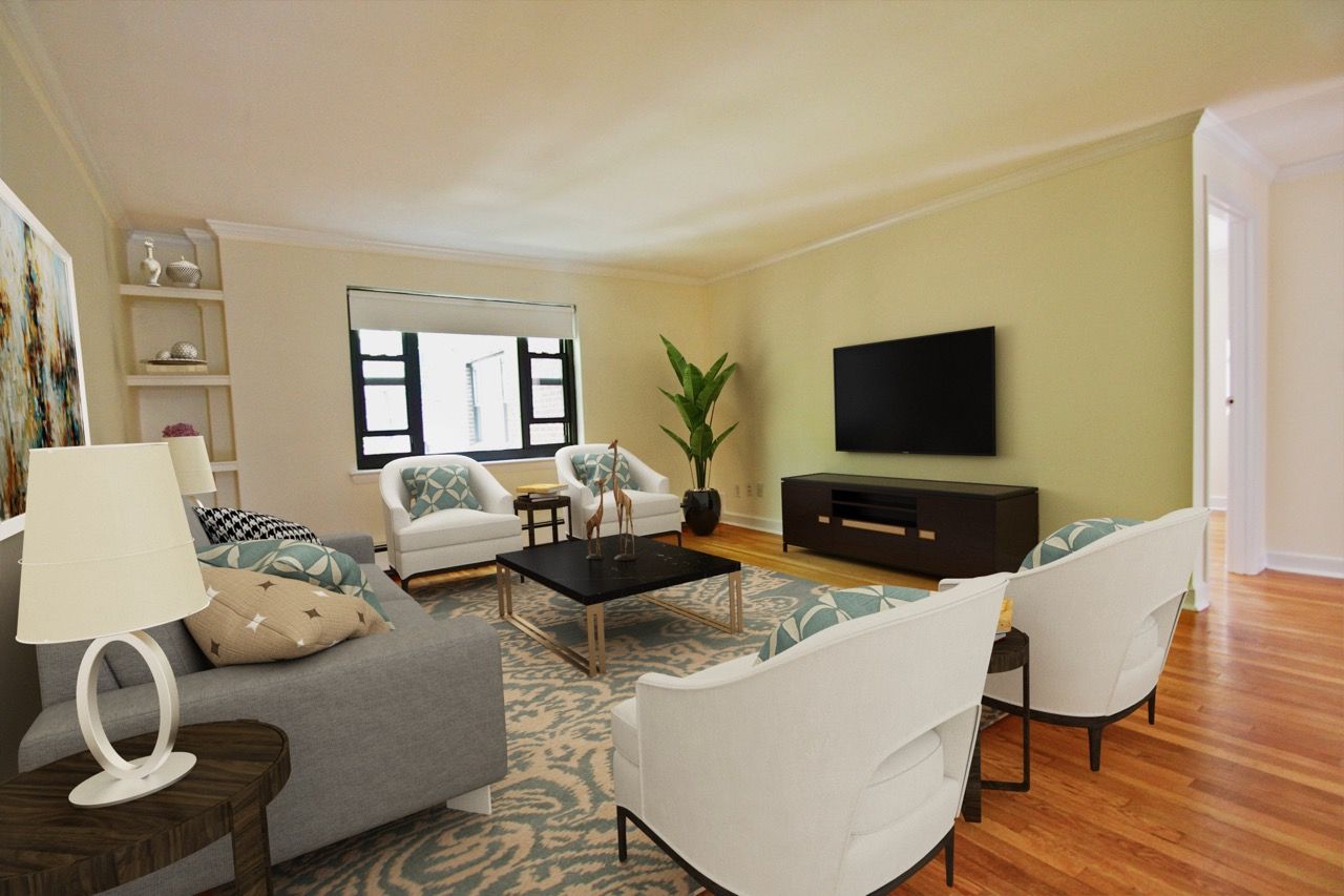 Living room in an apartment with white chairs around a black coffee table, gray sofa, TV on a stand, and hardwood floor.