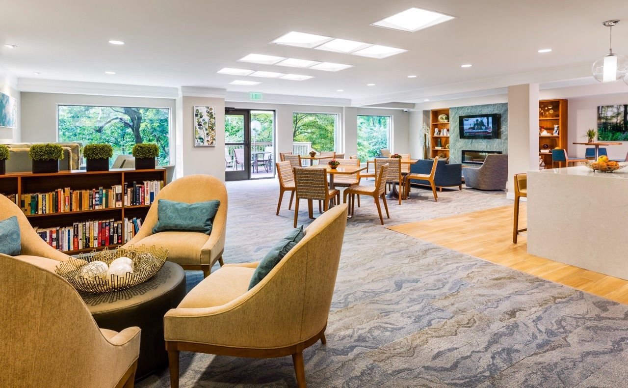 Bright apartment community lounge with beige seating, a bookshelf, and large windows.