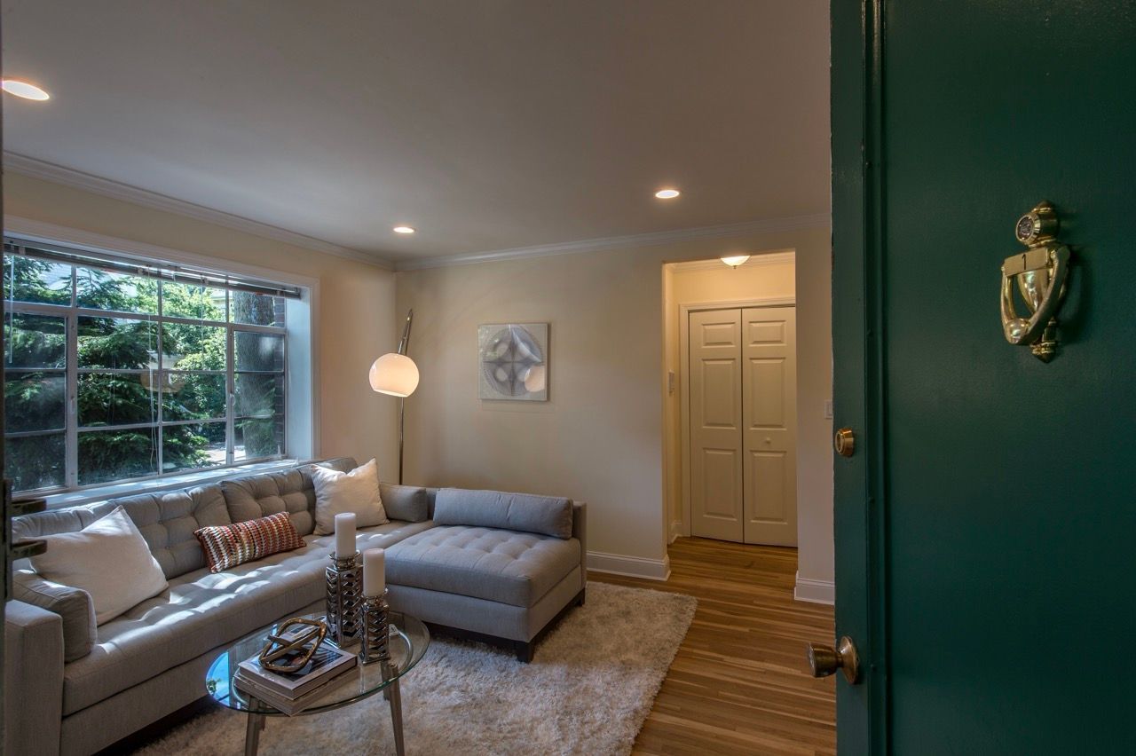 Living room in an apartment with a gray sectional sofa, glass coffee table, and a large window.