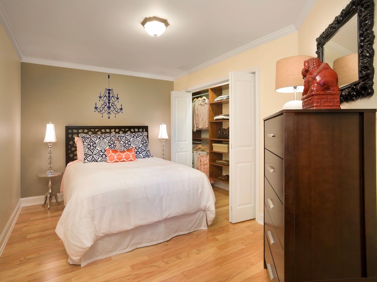 Bedroom in an apartment with a white comforter, navy patterned pillows, and an open closet.