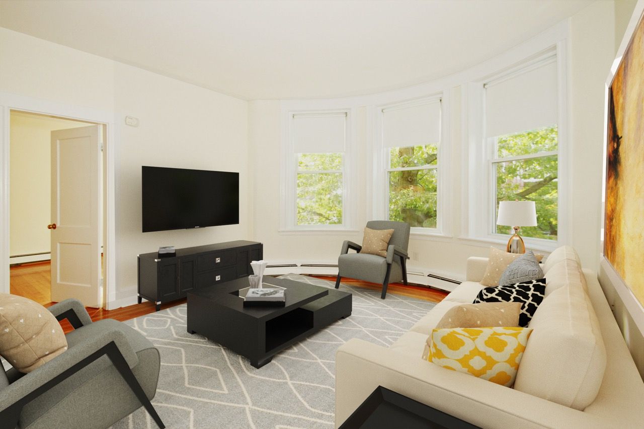 Living room in an apartment with a beige sofa, gray chairs, a black coffee table, TV, and large windows.