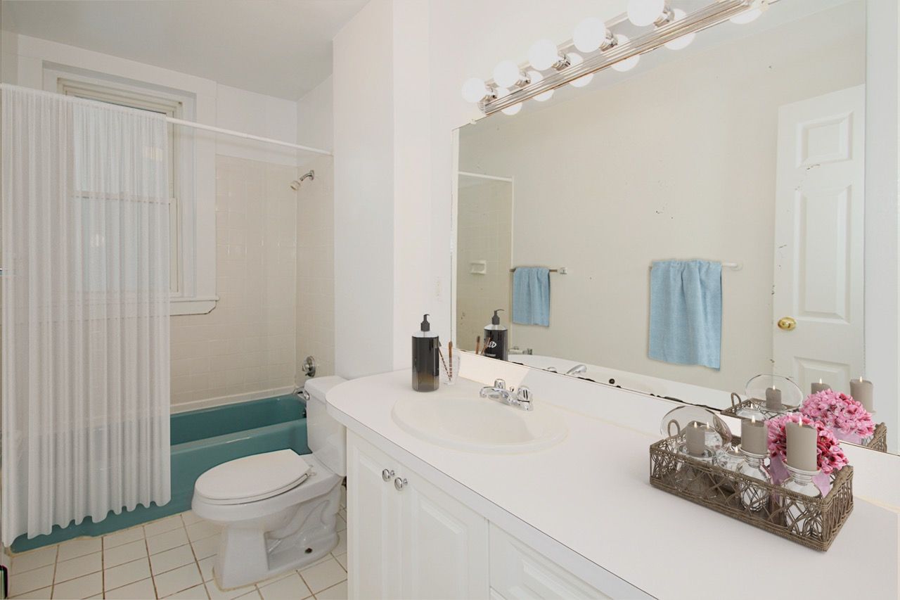 Bathroom with white vanity, large mirror, teal tub, and a shower curtain.