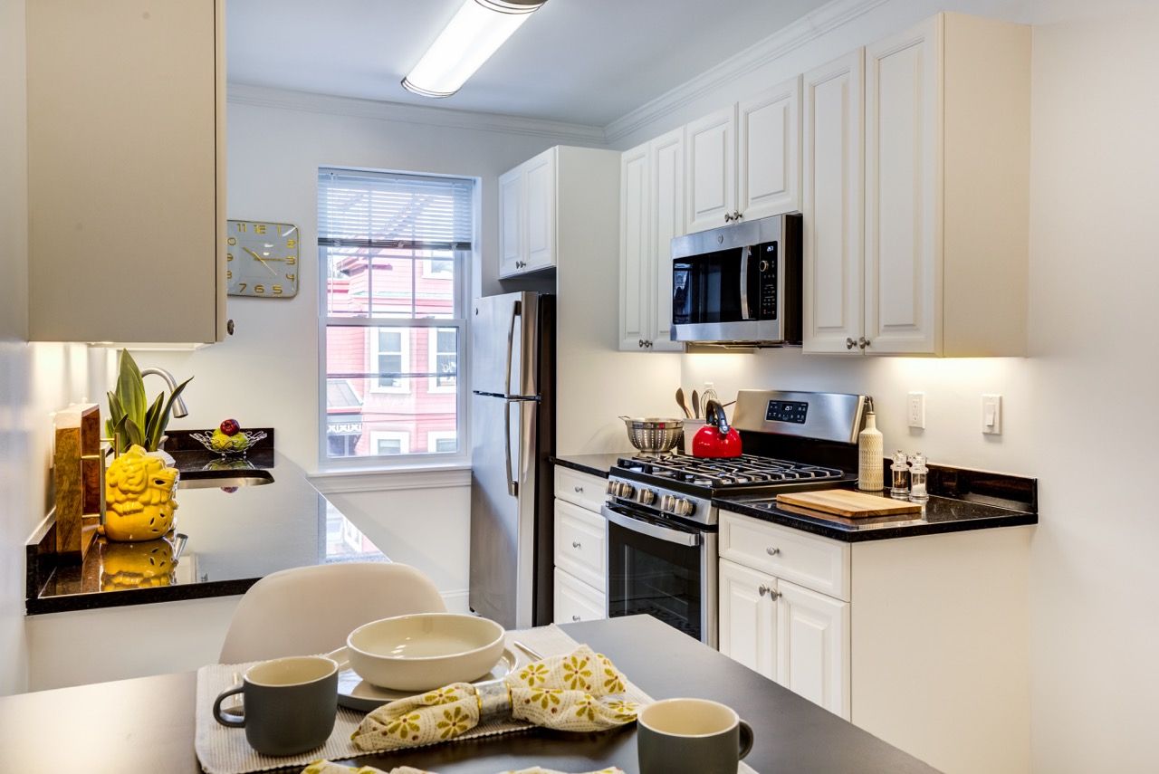 Bright kitchen with white cabinets, black counters, stainless steel appliances, and a window-side dining table.