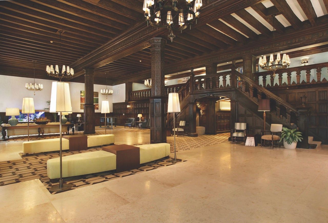 Lobby area with dark wood paneling, chandeliers, seating, and a grand staircase.