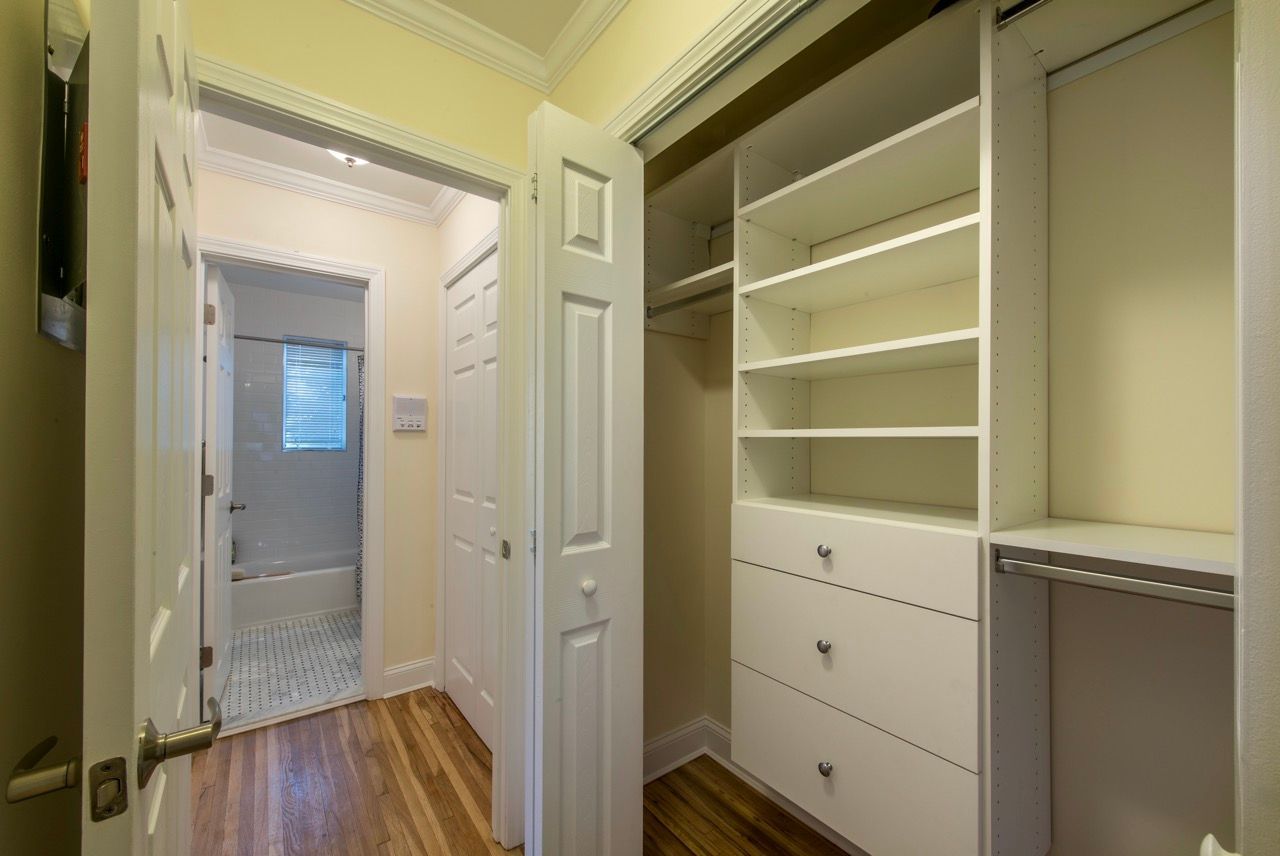 Open walk-in closet with white built-in shelves, drawers, and a hanging rod.