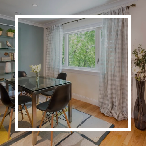 Modern dining room with a glass table, black chairs, and a large window with sheer curtains.