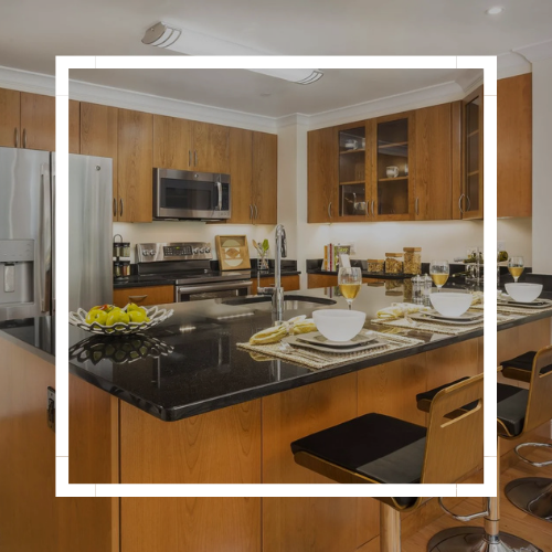 Modern kitchen with black granite island, wood cabinets, and a dining setup with bowls and glasses