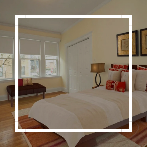 Bright bedroom with a bed, patterned bedding, two windows, and framed wall art