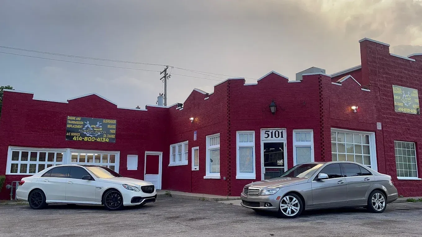 Red brick storefront with two parked cars in front and a cloudy sky overhead | Albeik Auto Service