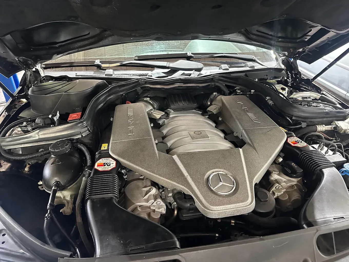 Mercedes-Benz engine bay with hood open, showing a silver V8 engine cover and surrounding components | Albeik Auto Service