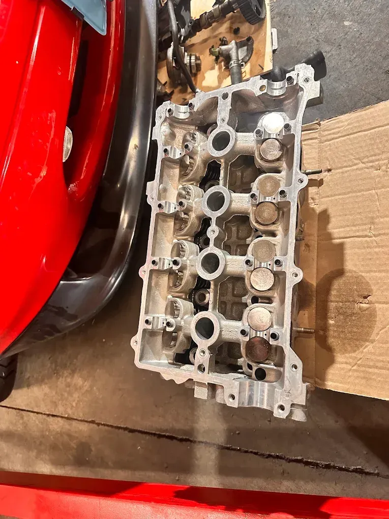 Damaged engine cylinder head on cardboard beside a red car wheel and black tire | Albeik Auto Service