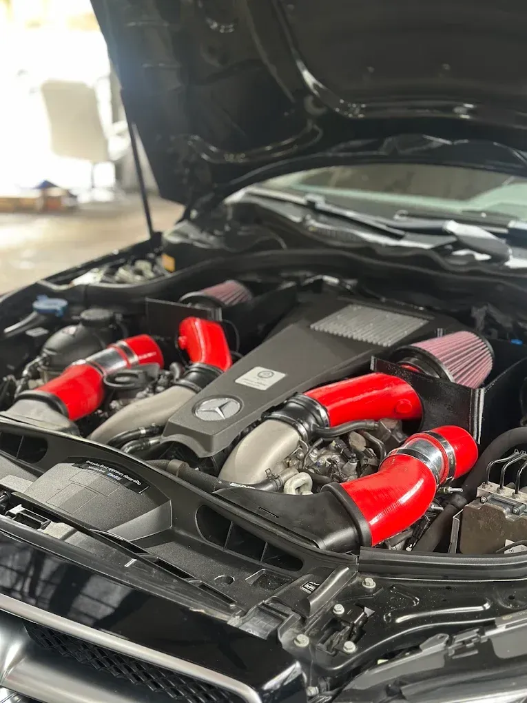Close-up of a car engine bay with red intake hoses and black components under an open hood | Albeik Auto Service