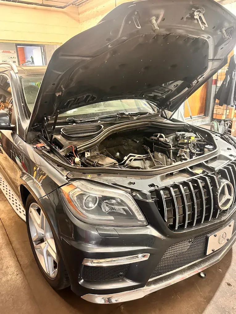 Black SUV with hood open in an indoor garage, showing the engine bay and front grille | Albeik Auto Service