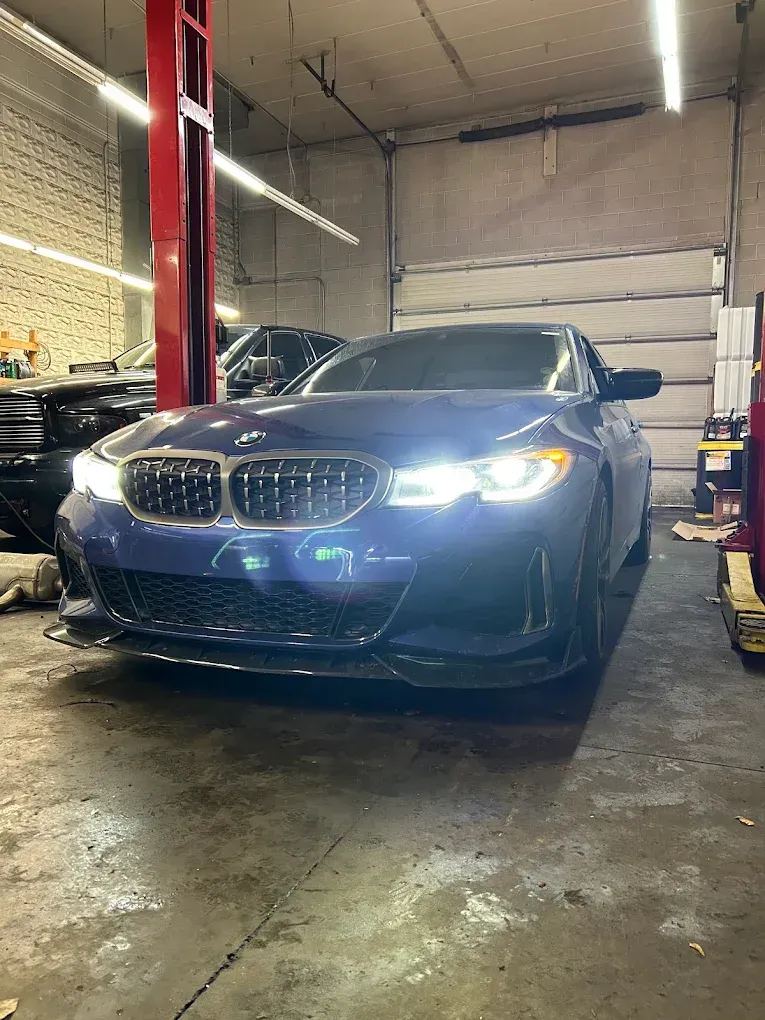 Blue BMW sedan in a garage, headlights on, parked on a wet concrete floor | Albeik Auto Service