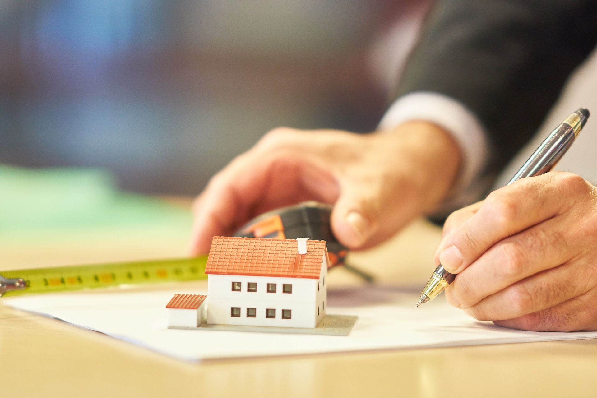 Mani che disegnano il progetto di una casa con matita e metro su una scrivania
