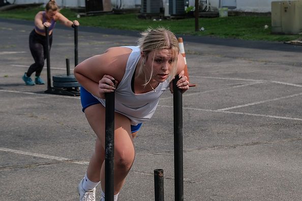 Athlete pushes a sled during an outdoor workout, leaning forward on a paved lot.