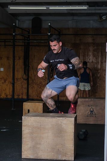 Man jumping onto a wooden box in CrossFit Bohica in Goldsboro, NC, with another person and gym equipment in the background