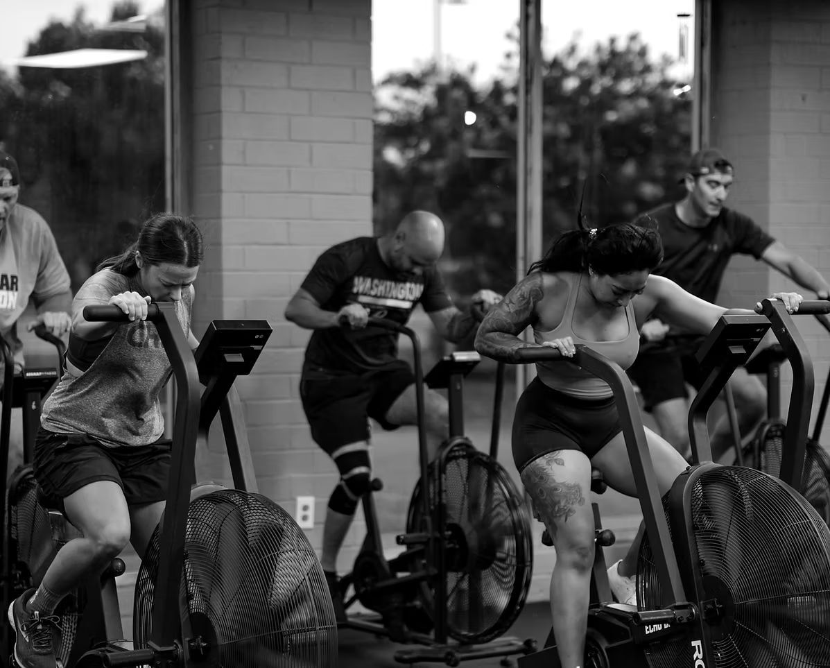 People exercising on stationary bikes in CrossFit Bohica in Goldsboro, NC, leaning forward during a workout.
