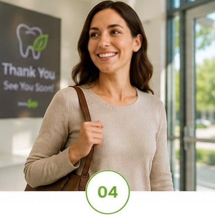 Woman smiling in a clinic lobby, wearing a beige sweater and shoulder bag, with a “Thank You, See You Soon” sign behind her