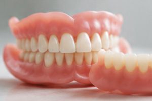 Two realistic pink dentures with white teeth on a light surface