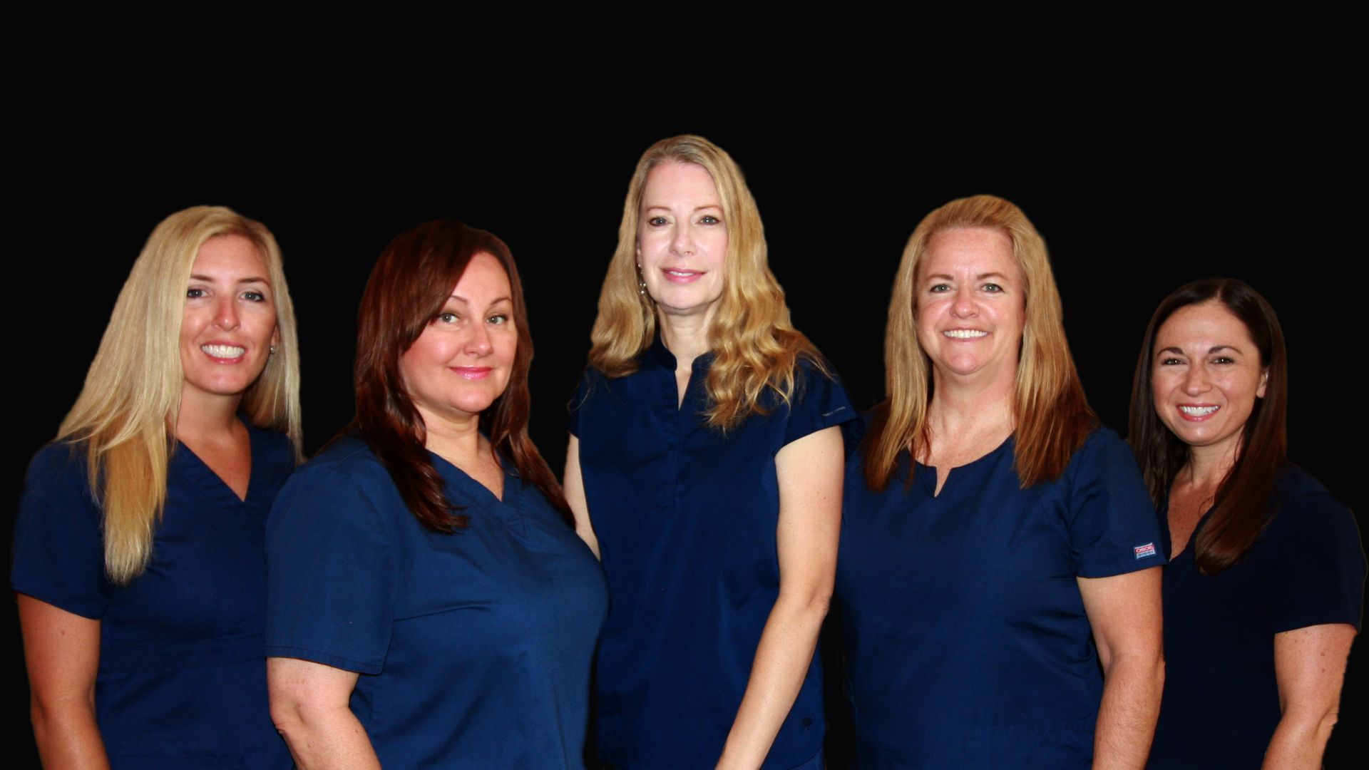 Five people stand side by side indoors, wearing matching navy shirts and smiling at the camera.