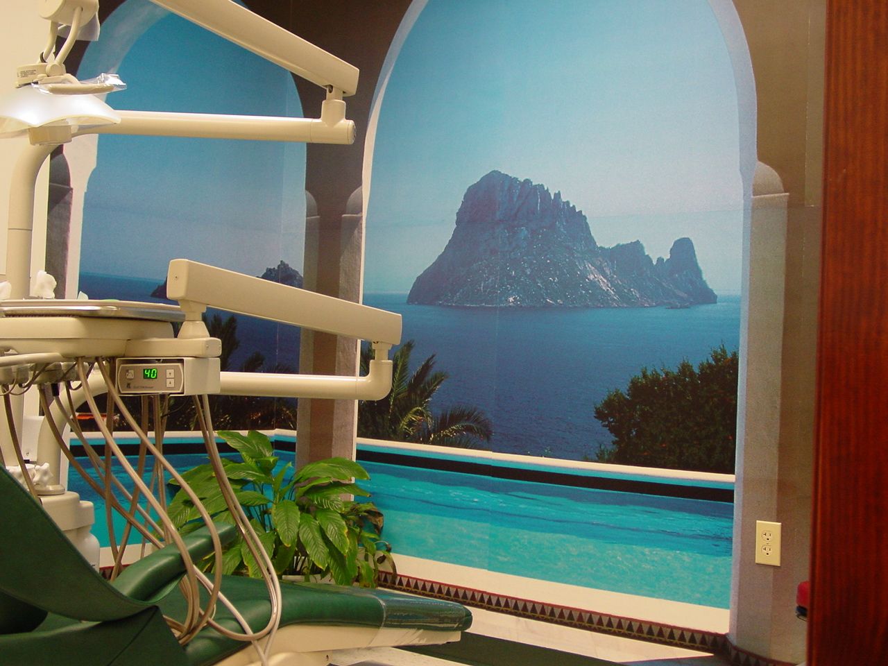 Modern dental exam room with mint-green chair, monitors, and large window