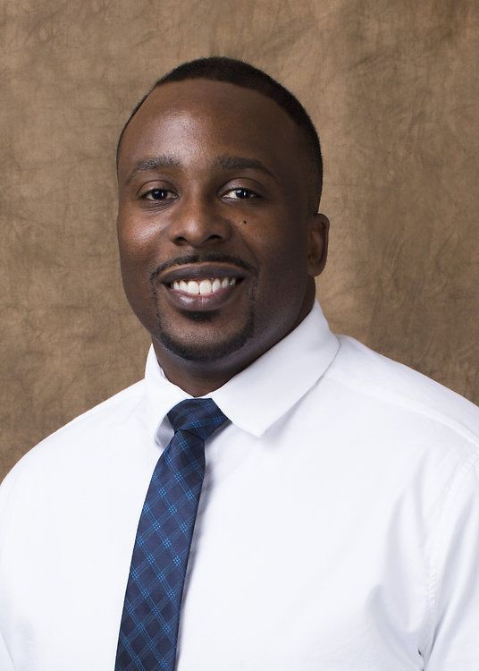 Portrait of a smiling man in a white shirt and blue tie against a brown backdrop
