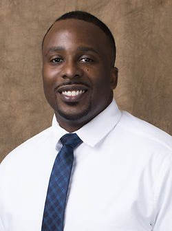 Portrait of a smiling man in a white shirt and blue tie against a brown background