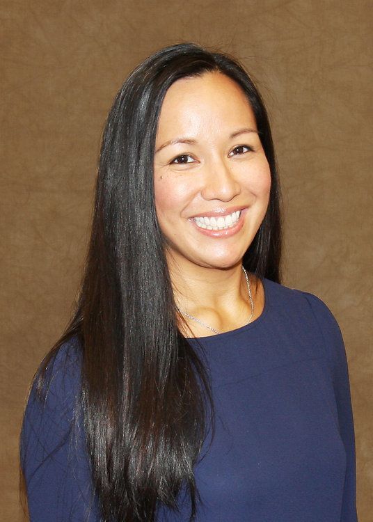 Smiling person with long dark hair wearing a navy top against a brown background