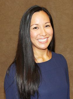 Smiling person in a navy top with long dark hair against a brown background