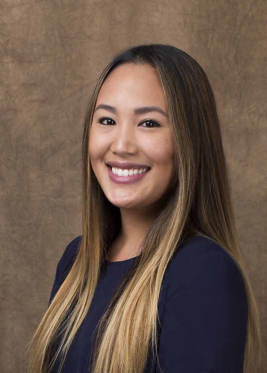 Smiling woman in a navy top against a textured brown studio backdrop
