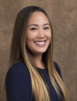 Smiling woman with long straight hair wearing a navy top against a brown backdrop
