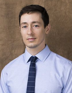 Portrait of a man in a light blue shirt and dark tie against a brown backdrop