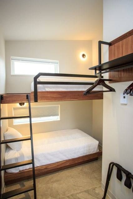 A modern room featuring a wooden bunk bed with white bedding, a ladder, and a wall-mounted garment rack.