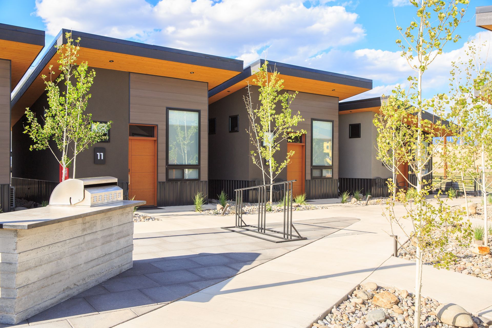 Modern single-story units with wood-paneled doors, flat roofs, and an outdoor grill area in a desert-style courtyard.