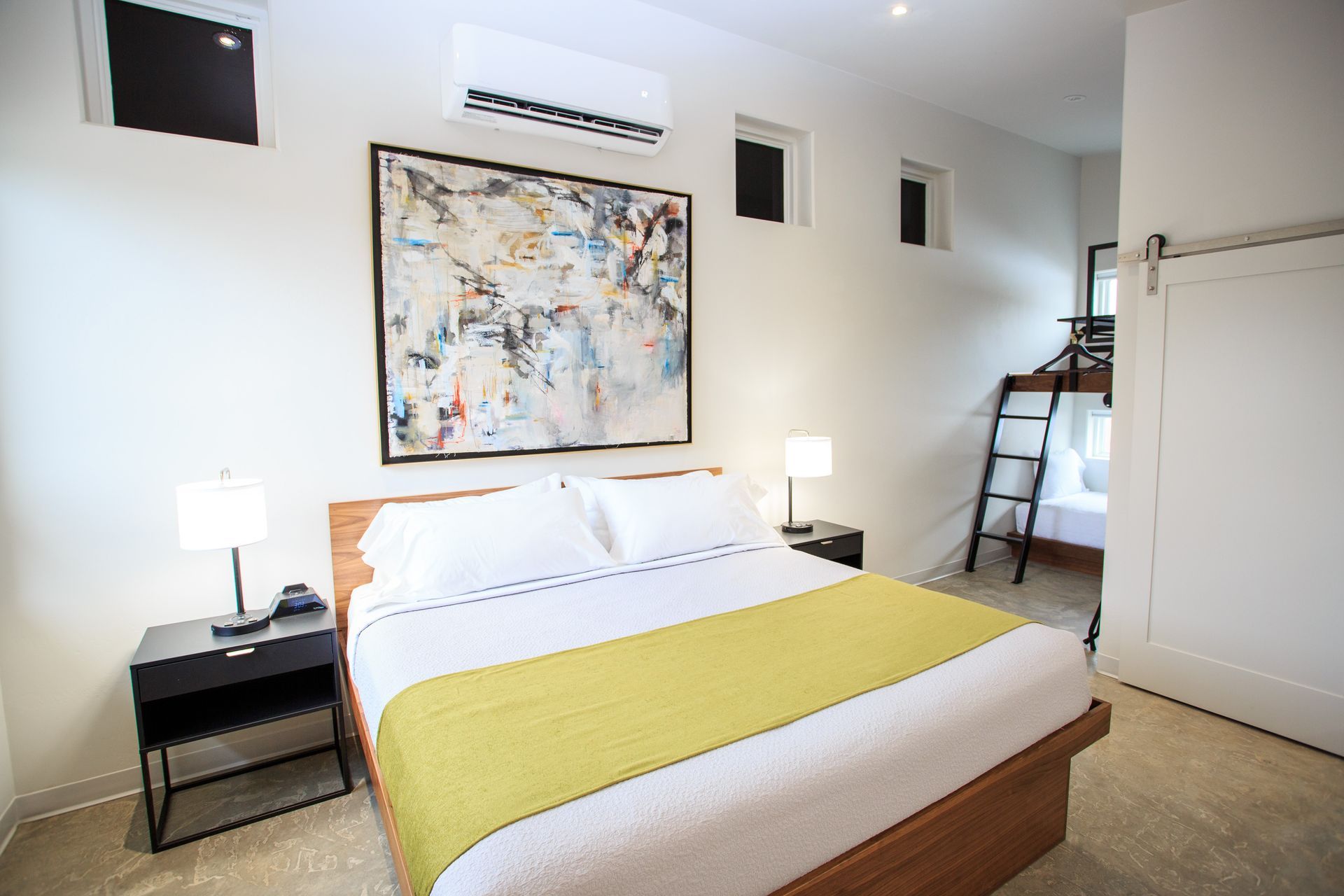 A bedroom with a king bed, yellow runner, two nightstands, framed artwork, and a bunk bed in the corner.