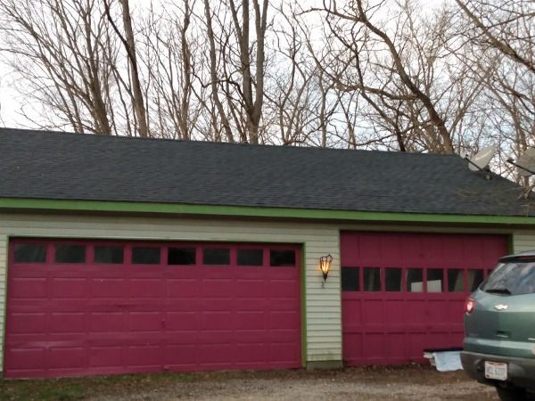 Red garage doors on a light yellow building, topped by a dark roof, trees in the background.