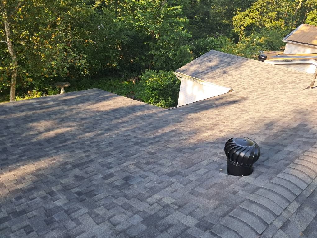 Asphalt shingle roof with a turbine vent, surrounded by trees. Asphalt shingle roof with a turbine vent, surrounded by trees.