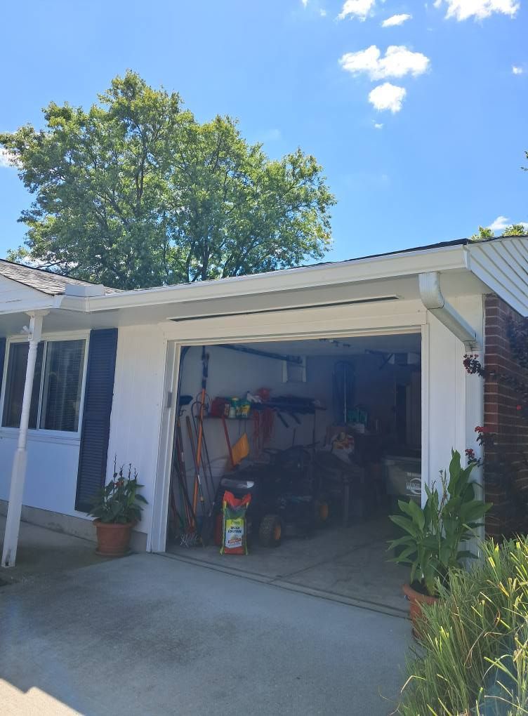 Garage with open door, various tools inside, white exterior, blue sky with tree in background.
