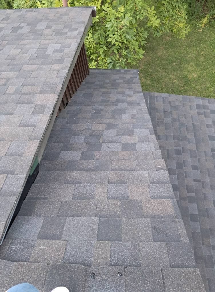 Overhead view of a roof with gray shingles, a wooden trim, and green grass in the background.