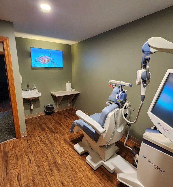 TMS therapy room with a reclining chair, monitor, sink, and wood flooring.