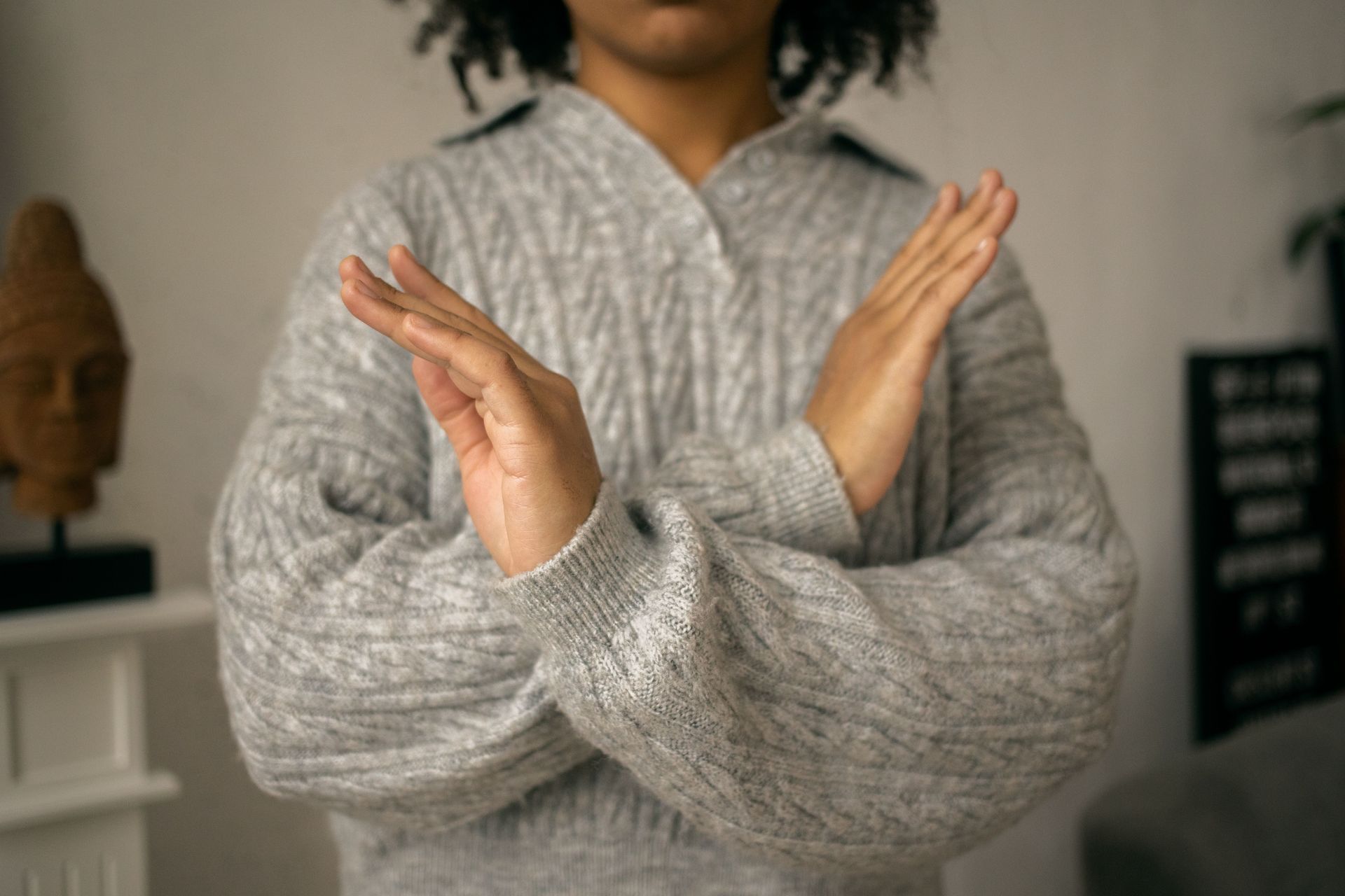 Person in a gray sweater crossing arms in front of their chest indoors.