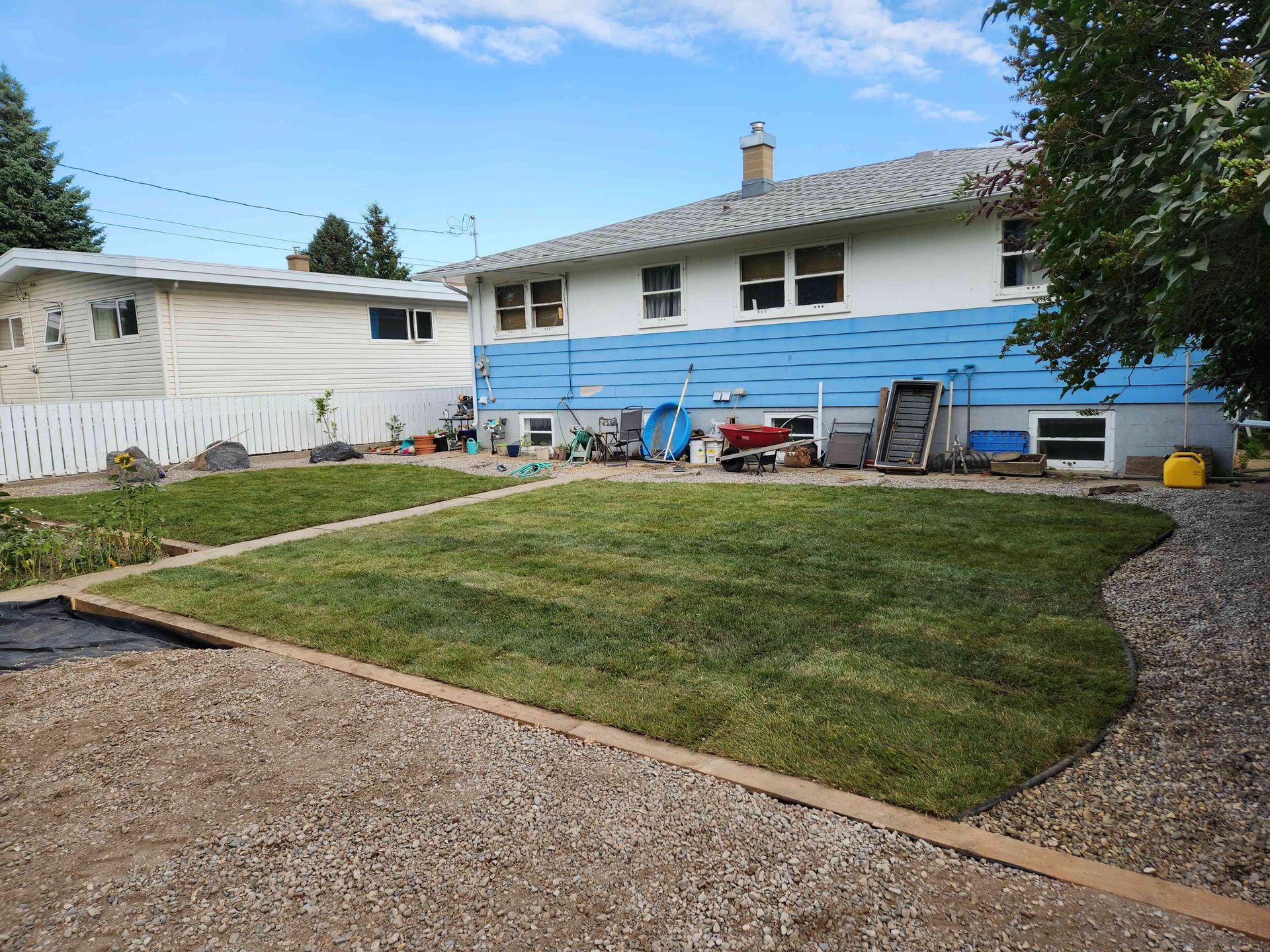 A backyard with a rectangular patch of newly laid green sod, bordered by light-colored landscaping gravel and a white fence.