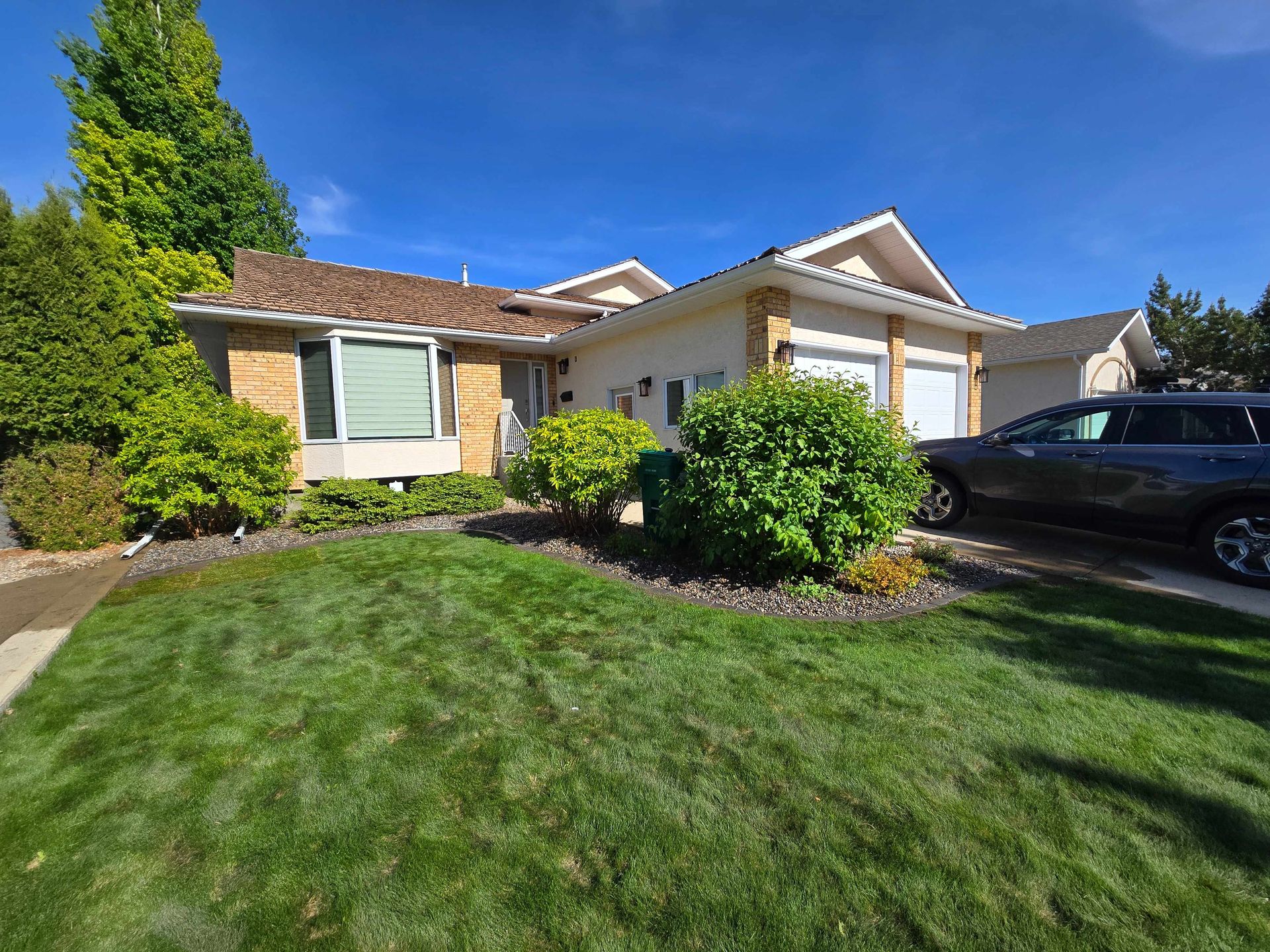 A beige, single-story house with a brown roof and a green lawn under a bright, sunny blue sky.