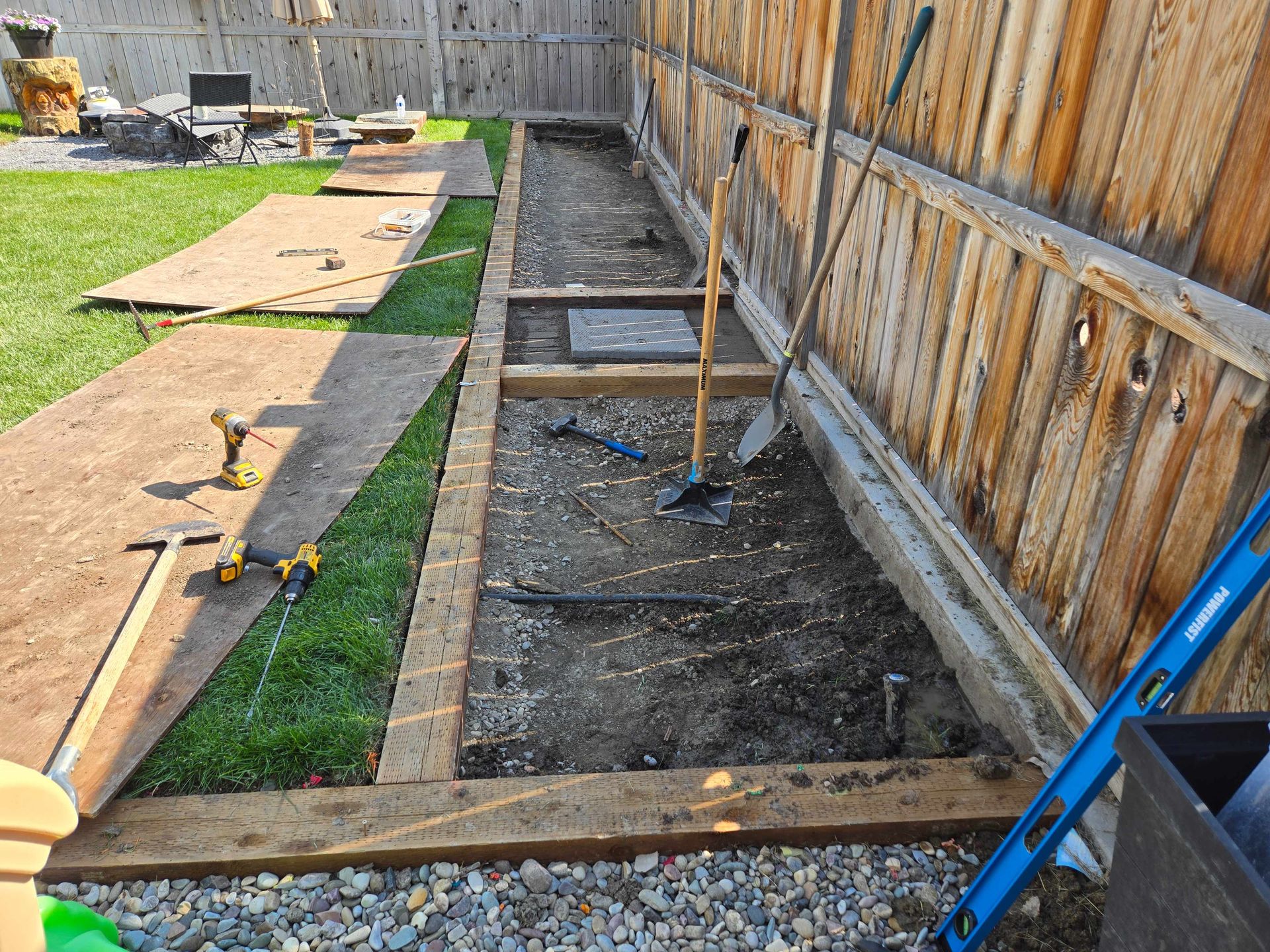 A backyard garden project with wooden landscape timbers, tools, and construction materials set against a wooden fence.