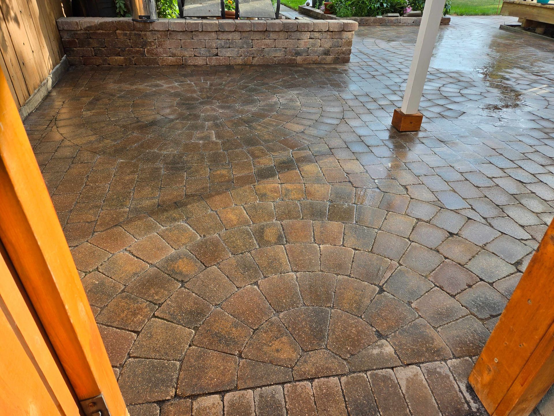 A patio area featuring interlocking, multi-toned brown pavers laid in a fan pattern, wet from recent rain.