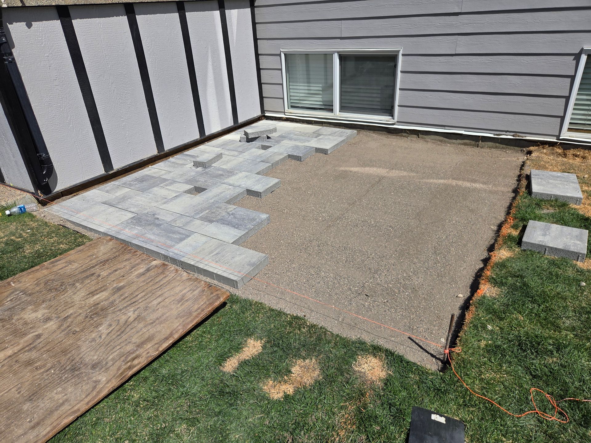 Backyard patio area with pavers, gravel, and grass beside a house window and siding